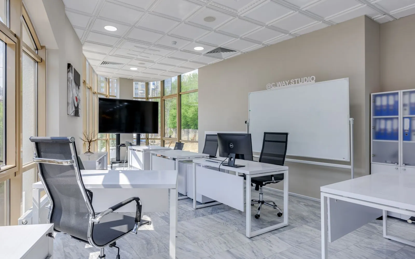 Bright office with white desks by tall windows